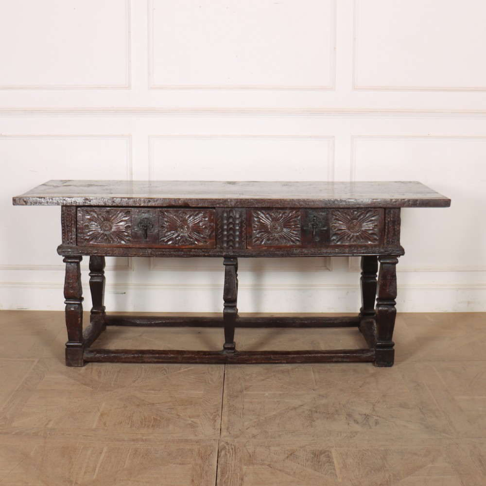 A 17th-century Spanish dark oak console table featuring carved drawer fronts with rosette motifs, turned legs, iron handles, and a box stretcher base.