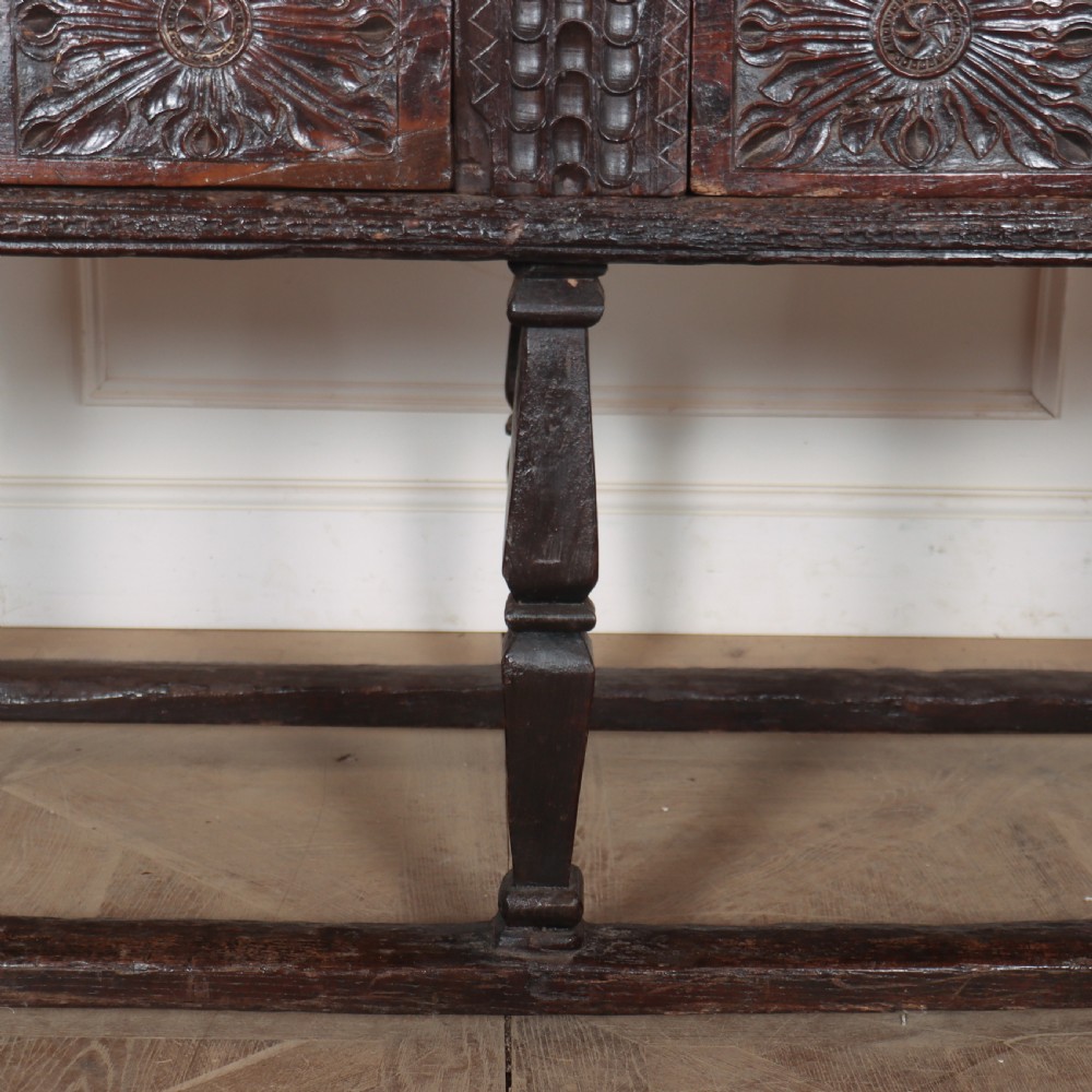 A 17th-century Spanish dark oak console table featuring carved drawer fronts with rosette motifs, turned legs, iron handles, and a box stretcher base. View V