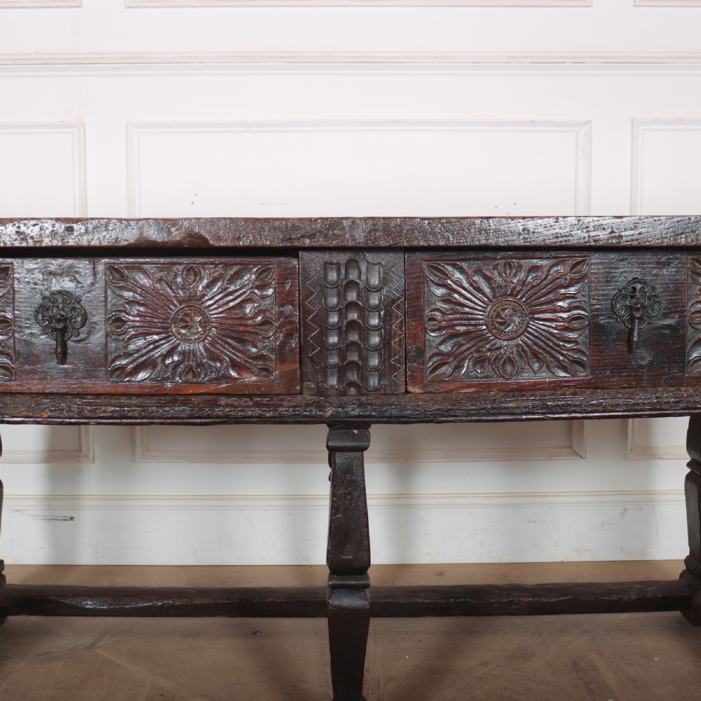 A 17th-century Spanish dark oak console table featuring carved drawer fronts with rosette motifs, turned legs, iron handles, and a box stretcher base. View VI