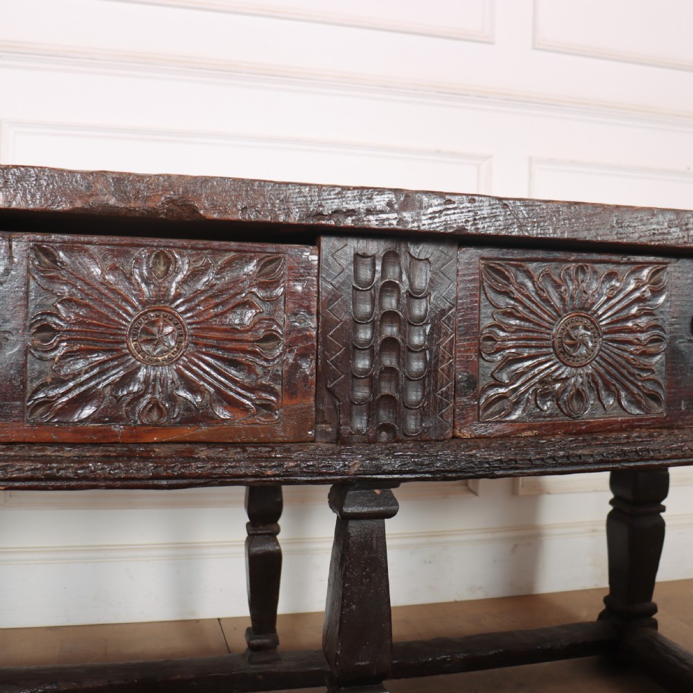 A 17th-century Spanish dark oak console table featuring carved drawer fronts with rosette motifs, turned legs, iron handles, and a box stretcher base. View X