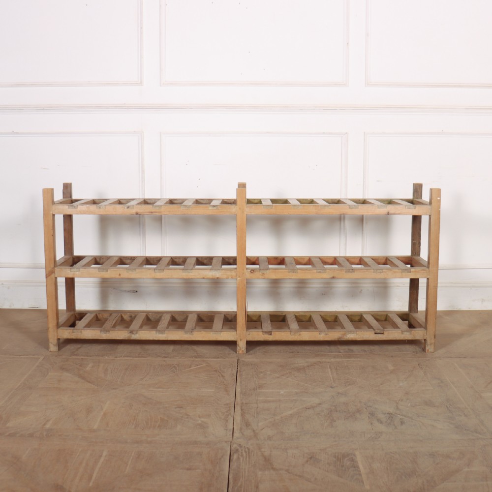A three-tier slatted pine shoe rack with vertical support posts and a natural unvarnished wood finish.