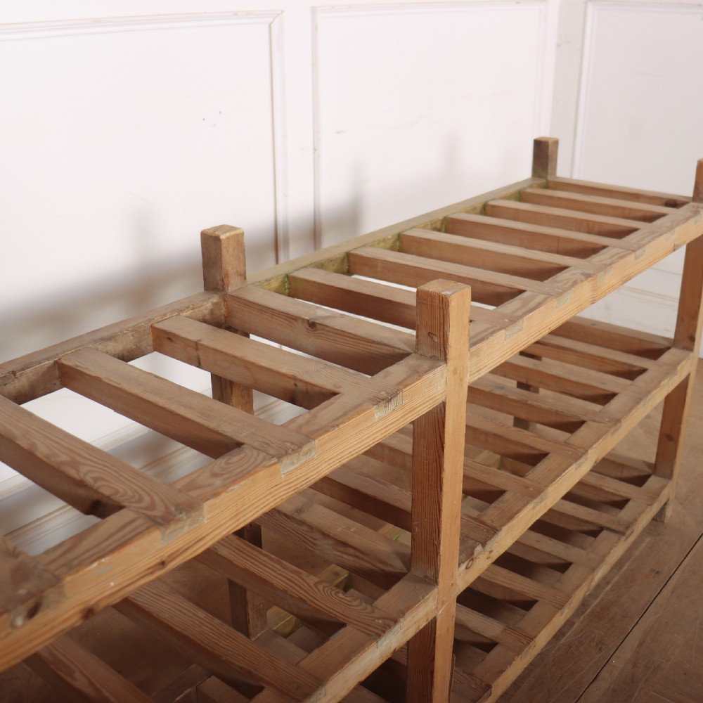 A three-tier slatted pine shoe rack with vertical support posts and a natural unvarnished wood finish. View VI