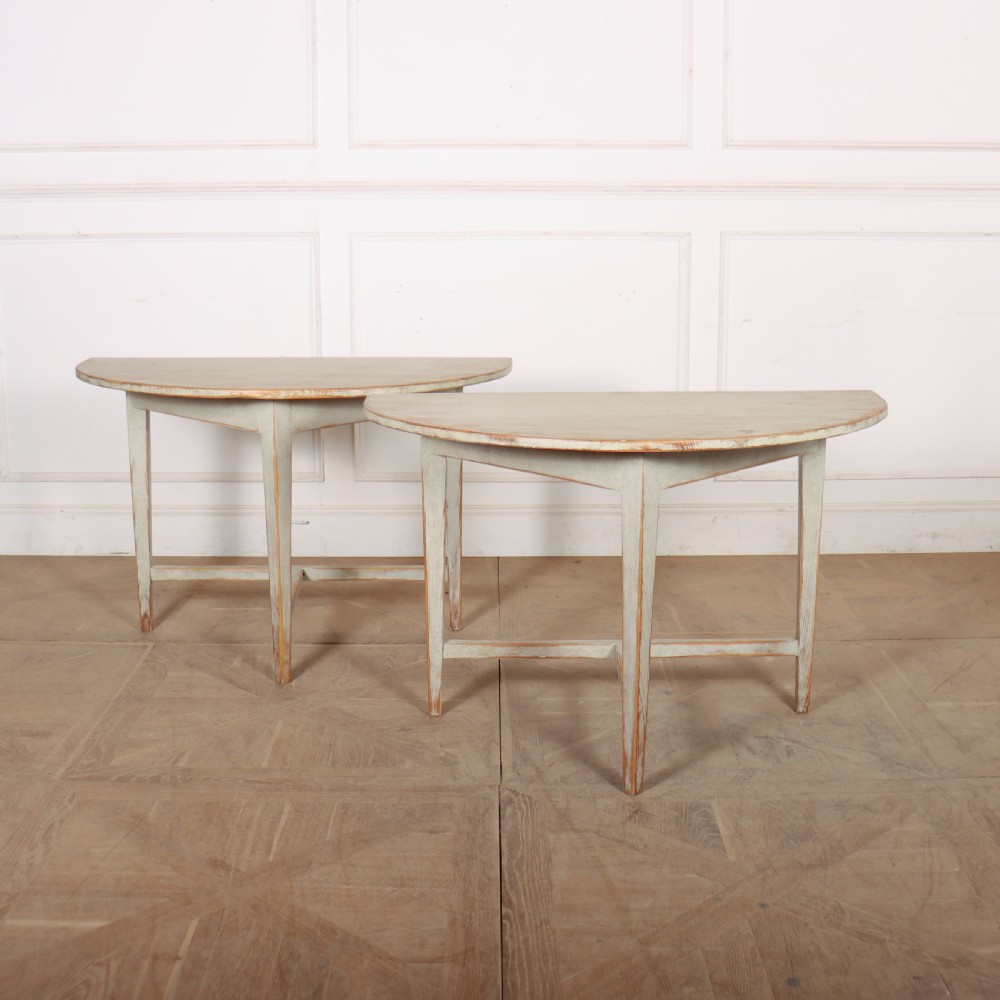 A pair of antique Swedish semi-circular console tables featuring a distressed pale grey painted finish, simple aprons, and straight tapered legs with stretchers.