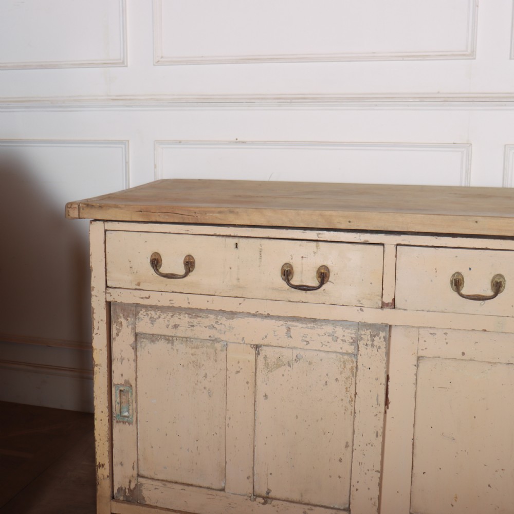 A long antique painted pine dresser base featuring four upper drawers with brass handles above panelled cupboard doors and a natural timber top. View II