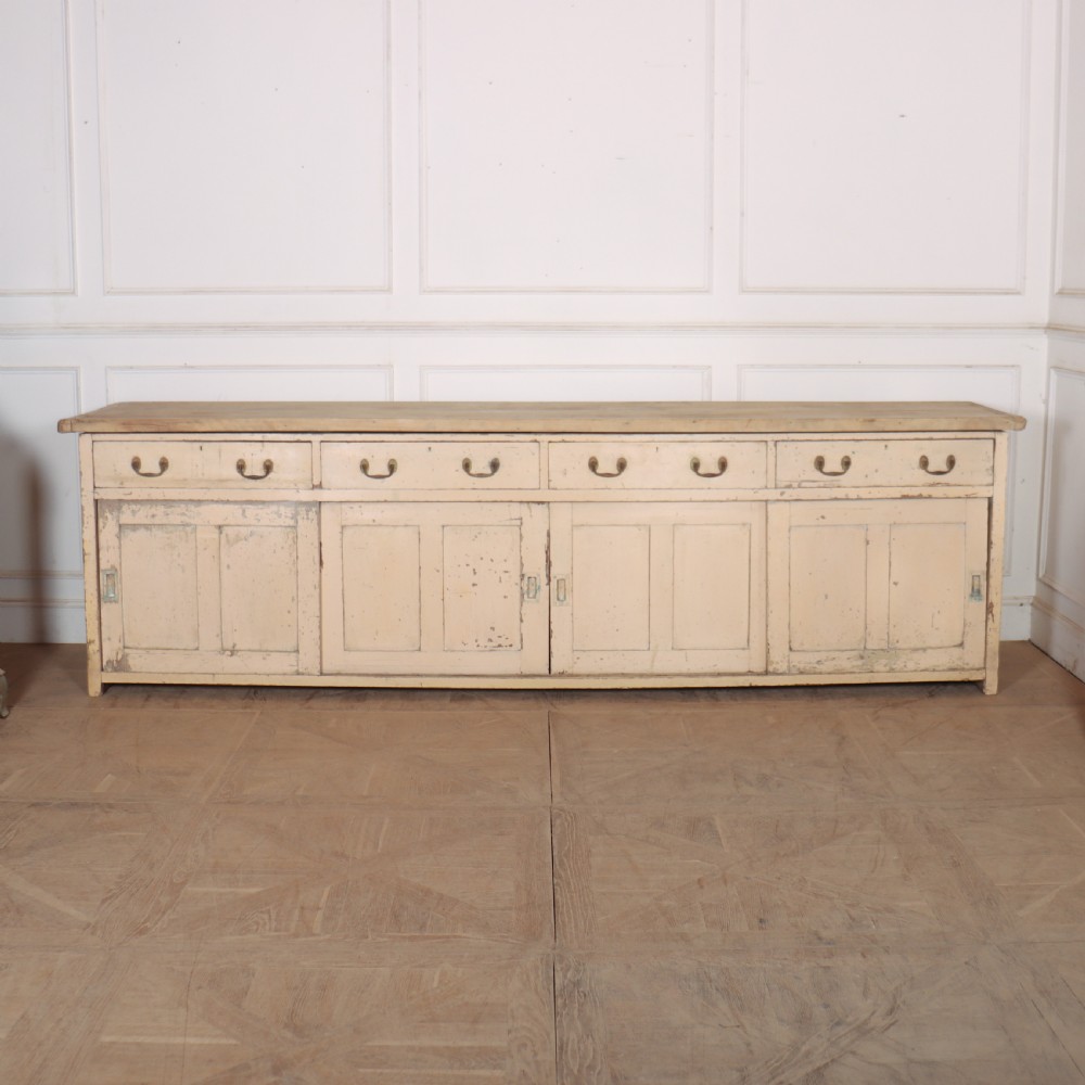 A long antique painted pine dresser base featuring four upper drawers with brass handles above panelled cupboard doors and a natural timber top. View III