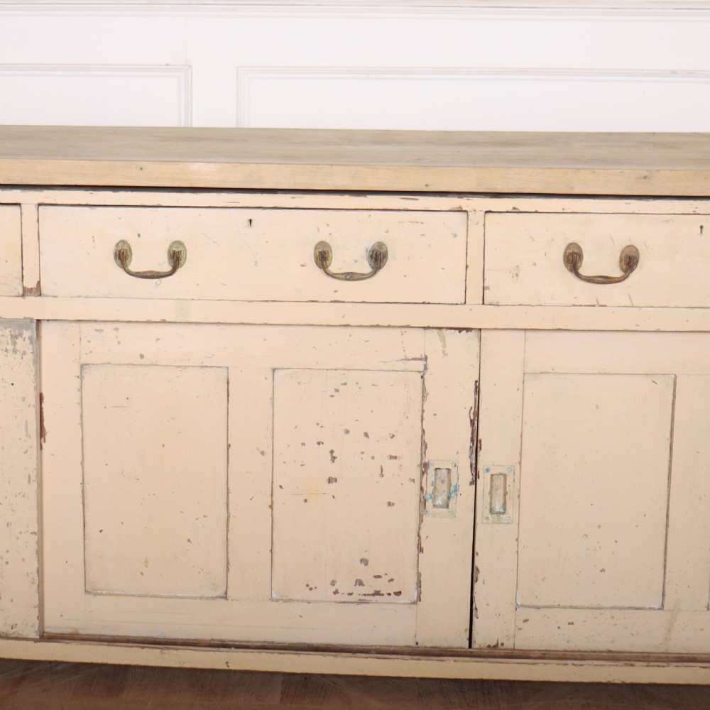 A long antique painted pine dresser base featuring four upper drawers with brass handles above panelled cupboard doors and a natural timber top. View IV