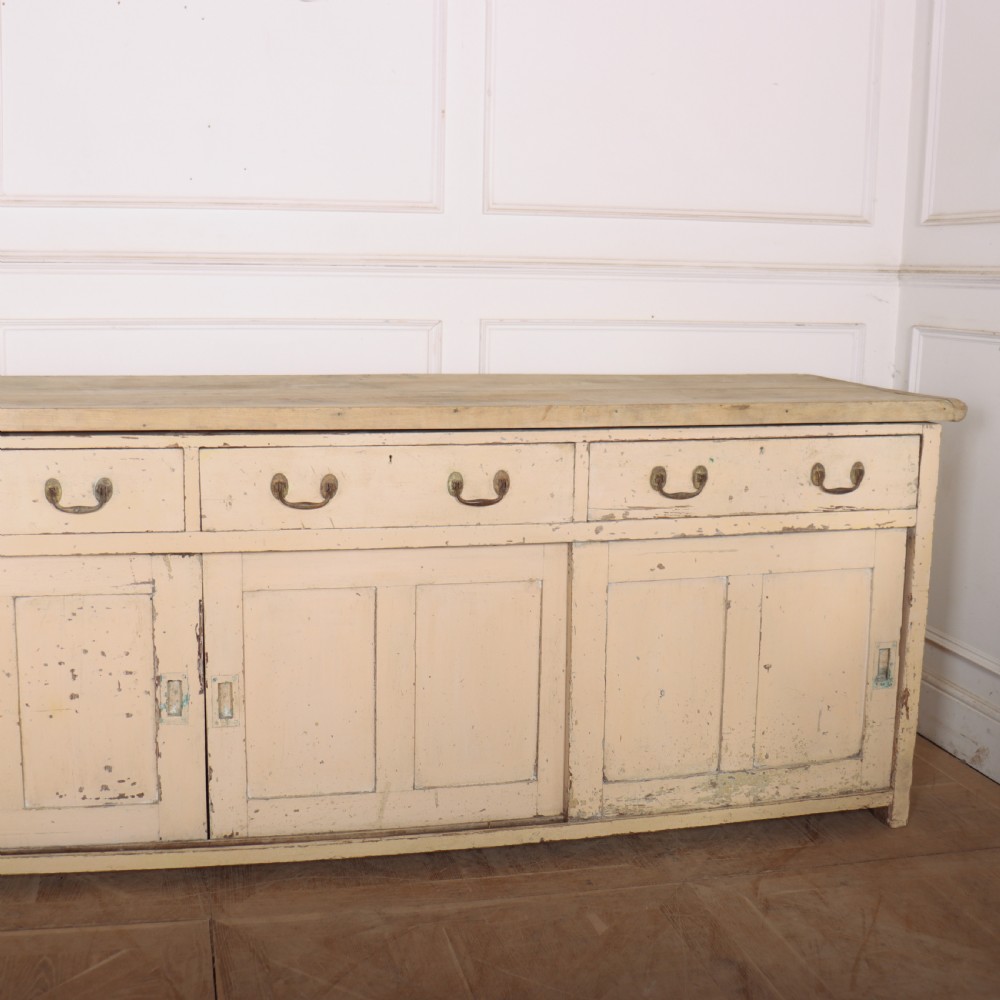 A long antique painted pine dresser base featuring four upper drawers with brass handles above panelled cupboard doors and a natural timber top. View V