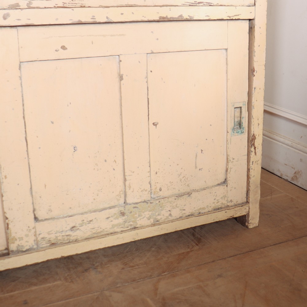 A long antique painted pine dresser base featuring four upper drawers with brass handles above panelled cupboard doors and a natural timber top. View VI