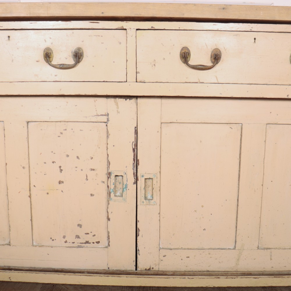 A long antique painted pine dresser base featuring four upper drawers with brass handles above panelled cupboard doors and a natural timber top. View VII
