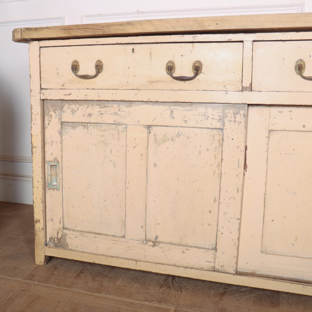 A long antique painted pine dresser base featuring four upper drawers with brass handles above panelled cupboard doors and a natural timber top. View VIII