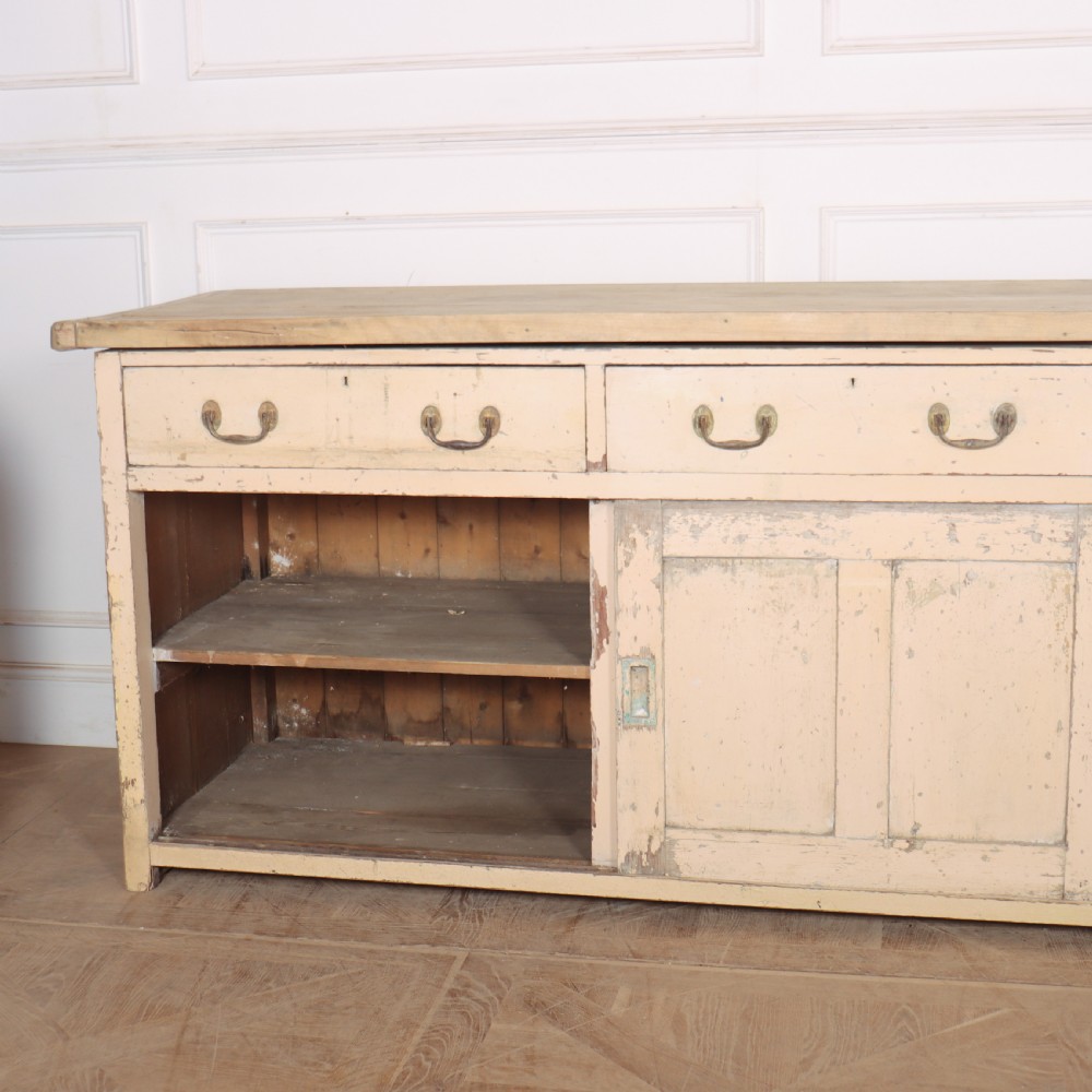 A long antique painted pine dresser base featuring four upper drawers with brass handles above panelled cupboard doors and a natural timber top. View IX