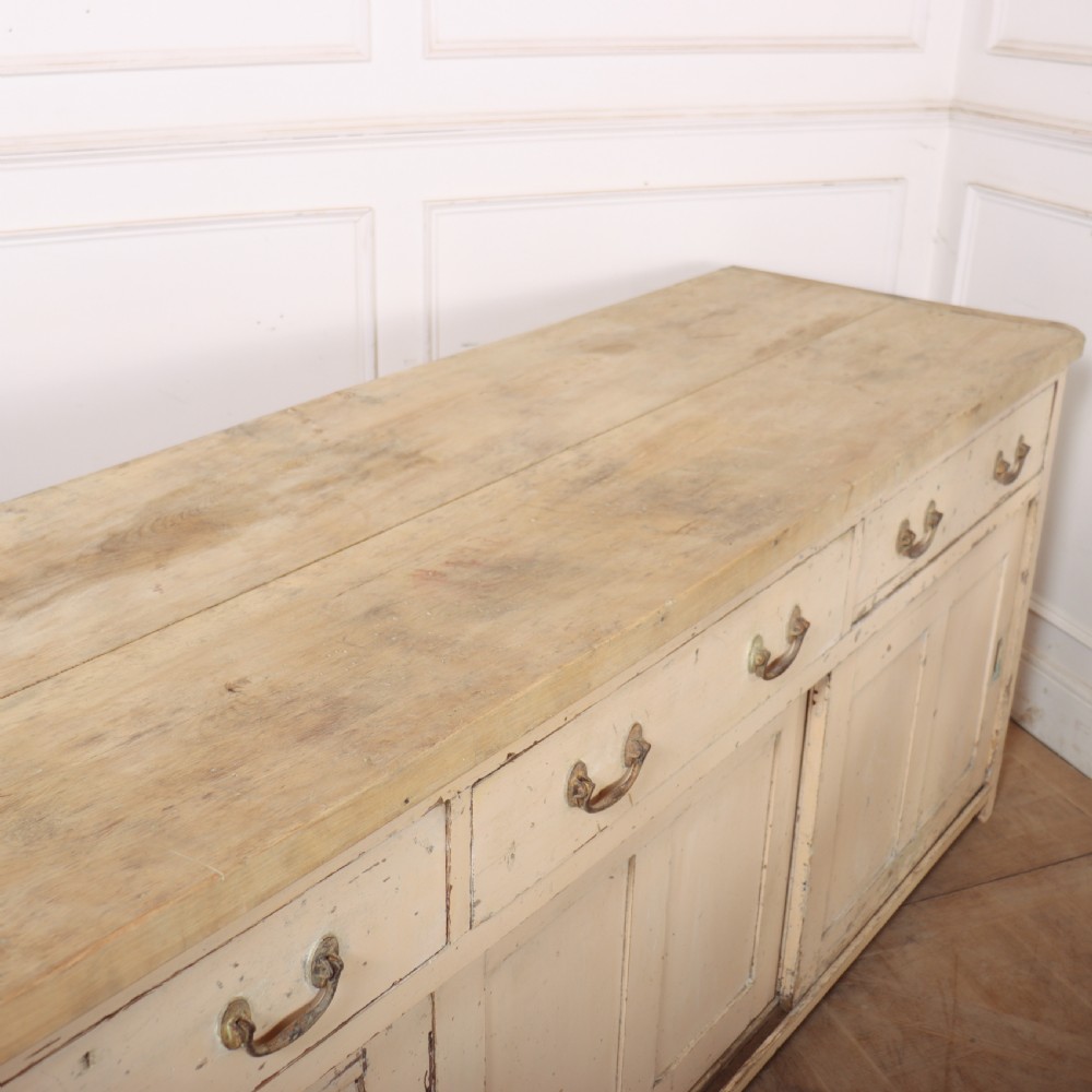 A long antique painted pine dresser base featuring four upper drawers with brass handles above panelled cupboard doors and a natural timber top. View XIII