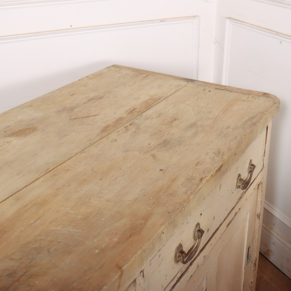 A long antique painted pine dresser base featuring four upper drawers with brass handles above panelled cupboard doors and a natural timber top. View XIV