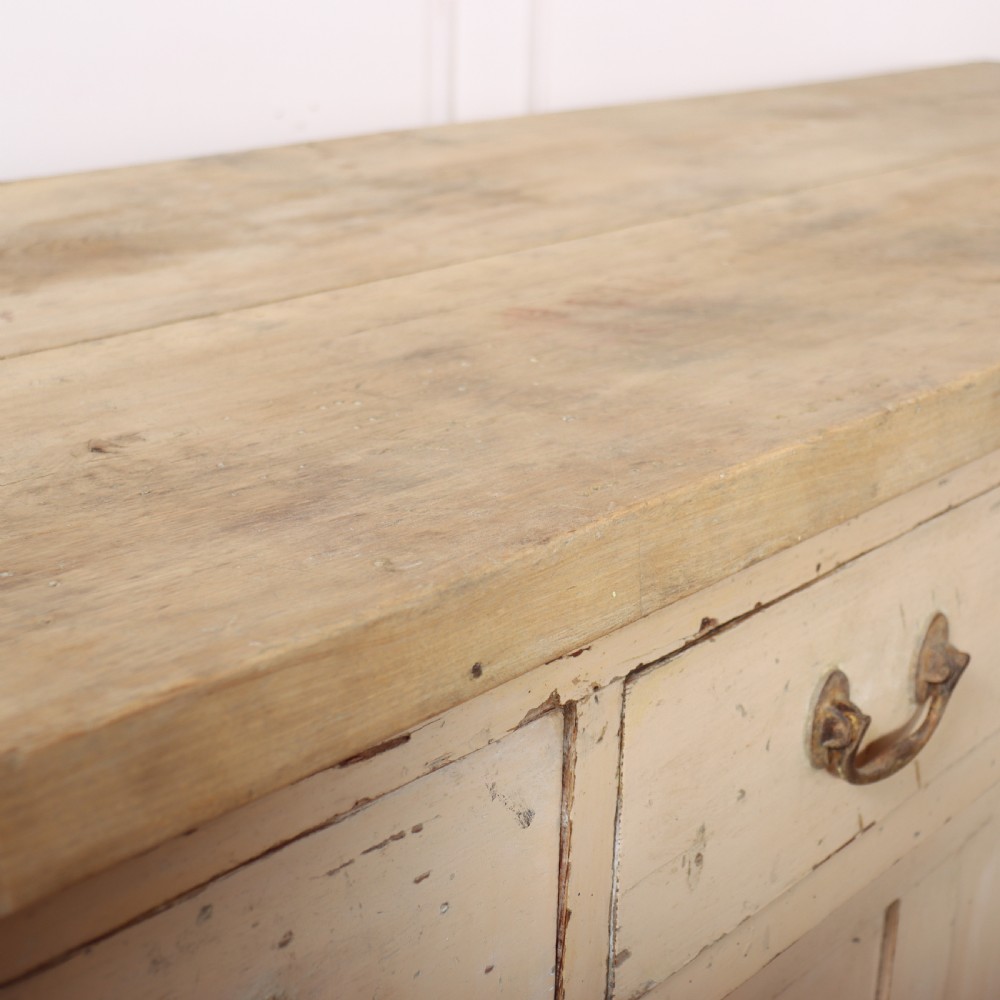 A long antique painted pine dresser base featuring four upper drawers with brass handles above panelled cupboard doors and a natural timber top. View XV