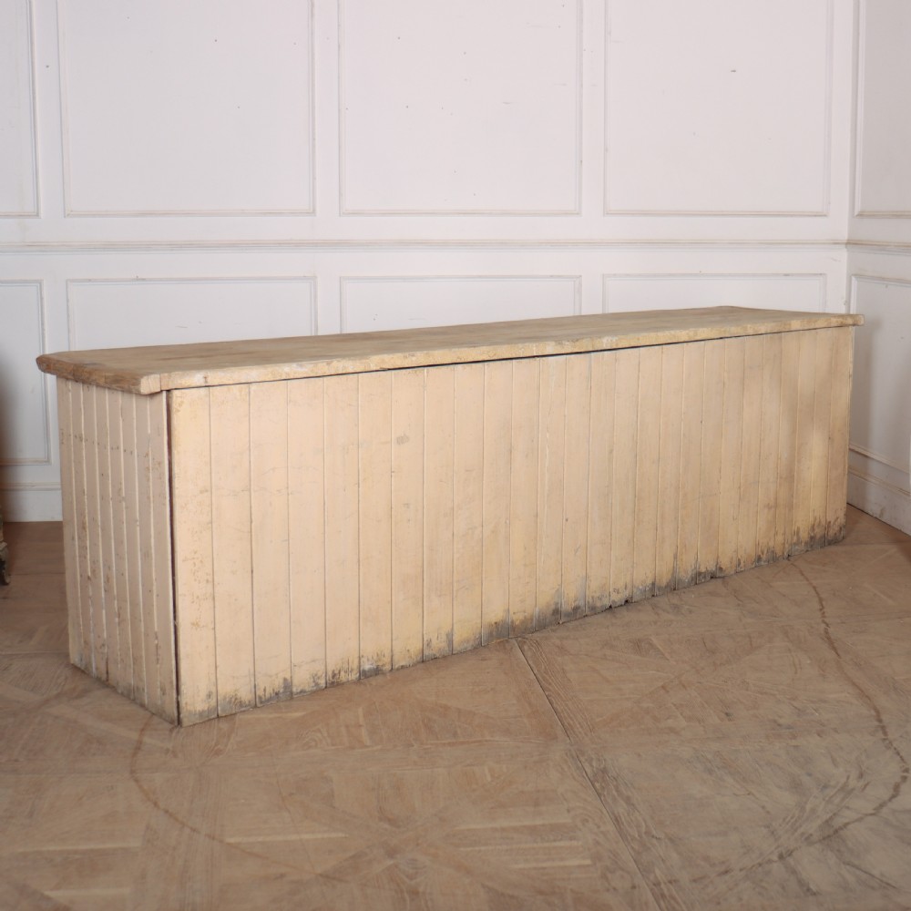 A long antique painted pine dresser base featuring four upper drawers with brass handles above panelled cupboard doors and a natural timber top. View XVI