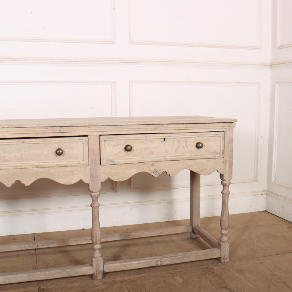 An English bleached oak dresser base featuring three drawers with brass knob handles, a scalloped apron, and turned legs connected by a stretcher base. View IV