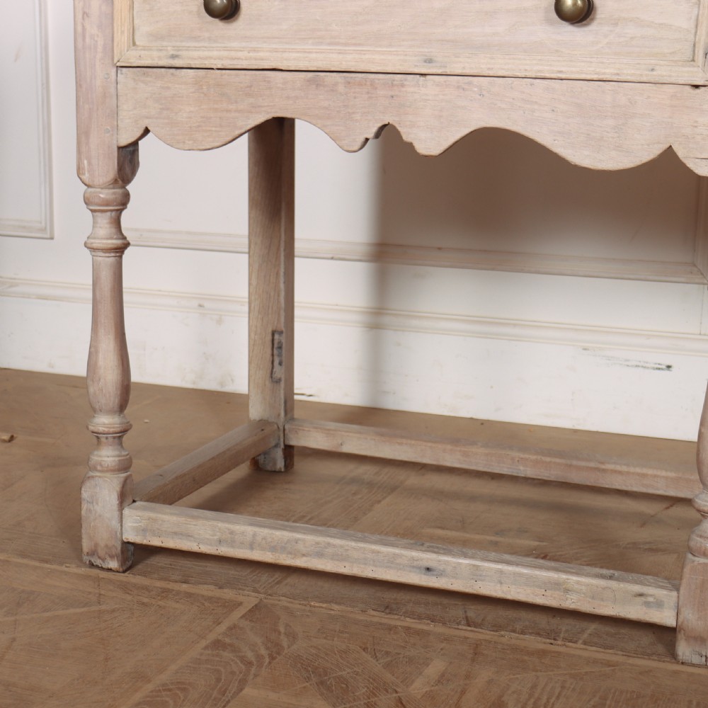 An English bleached oak dresser base featuring three drawers with brass knob handles, a scalloped apron, and turned legs connected by a stretcher base. View V