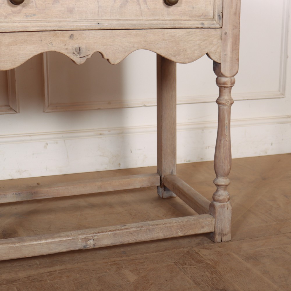 An English bleached oak dresser base featuring three drawers with brass knob handles, a scalloped apron, and turned legs connected by a stretcher base. View VI