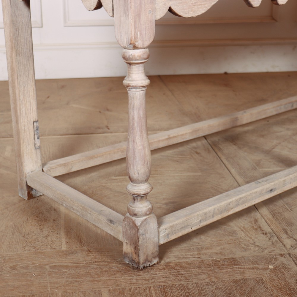 An English bleached oak dresser base featuring three drawers with brass knob handles, a scalloped apron, and turned legs connected by a stretcher base. View VIII