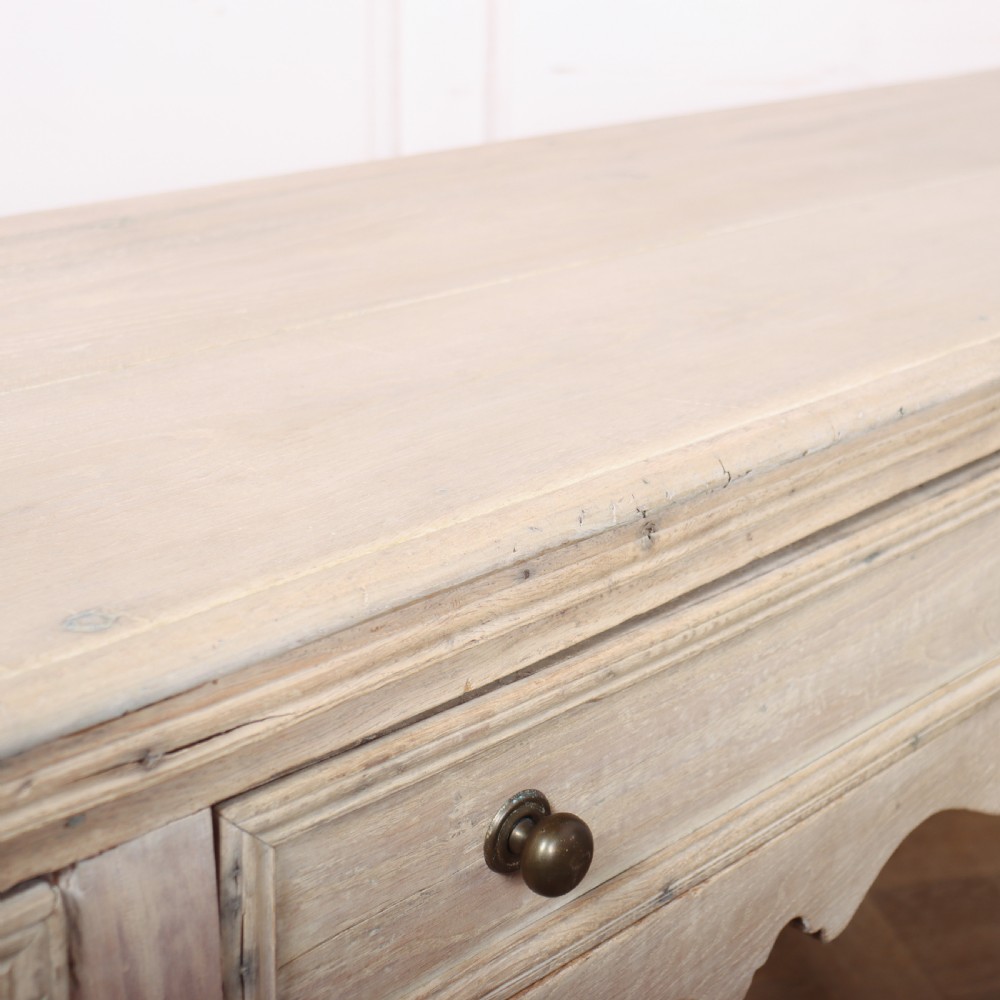 An English bleached oak dresser base featuring three drawers with brass knob handles, a scalloped apron, and turned legs connected by a stretcher base. View XII