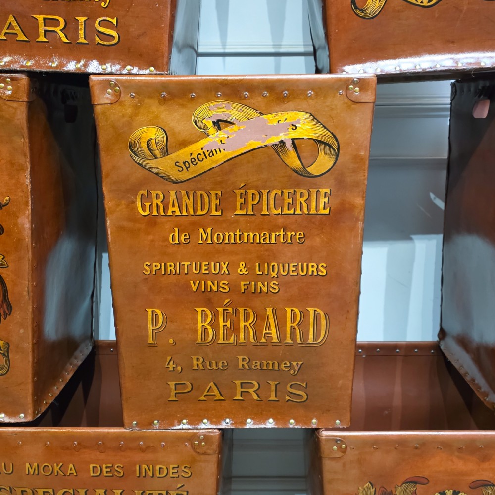 A collection of warm brown studded leather storage bins decorated with gilded French typography and heraldic crests. View X