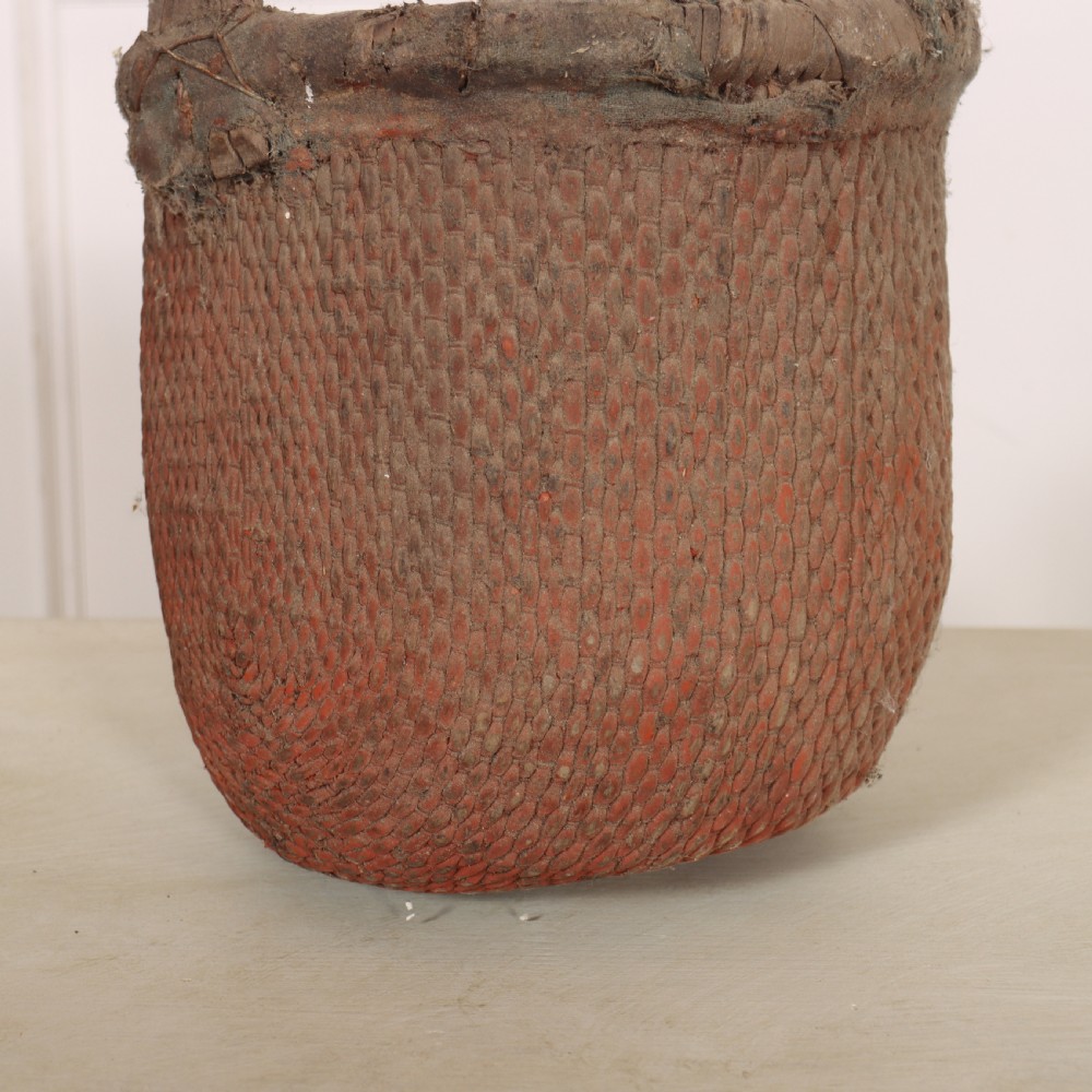 An antique English woven basket featuring a terracotta red painted finish, a structured rim, and a sturdy upright handle. View II