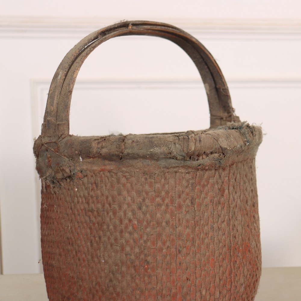 An antique English woven basket featuring a terracotta red painted finish, a structured rim, and a sturdy upright handle. View III