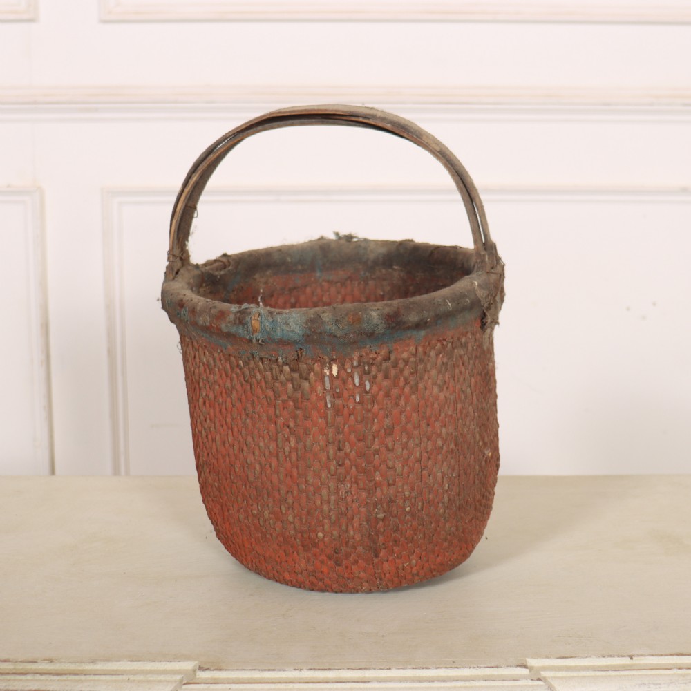 An antique English woven basket featuring a terracotta red painted finish, a structured rim, and a sturdy upright handle. View IV
