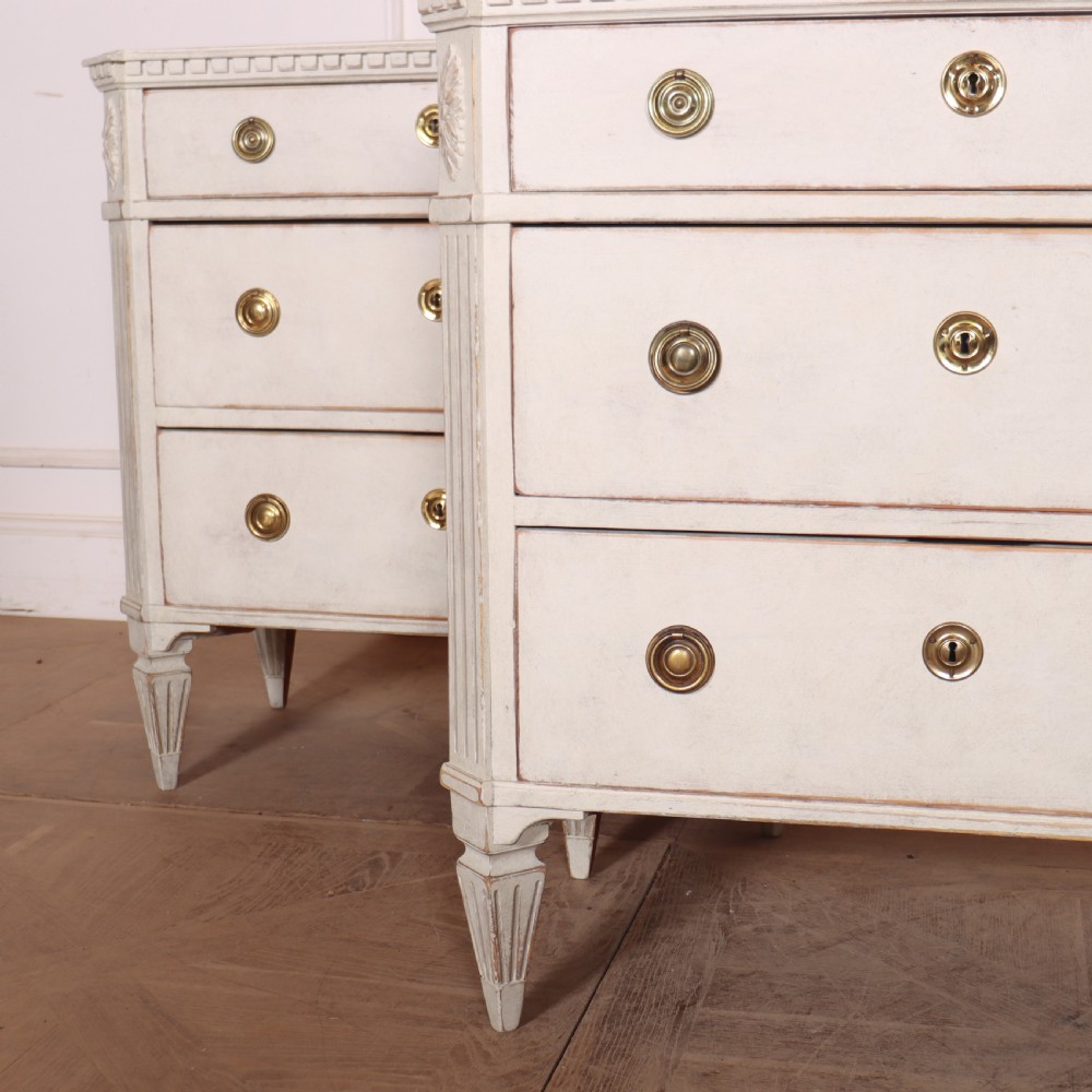 A pair of Swedish Gustavian style off-white painted commodes featuring three drawers each, brass hardware, fluted sides, and square tapered feet. View III