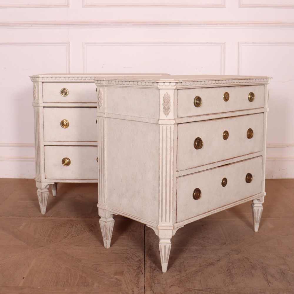 A pair of Swedish Gustavian style off-white painted commodes featuring three drawers each, brass hardware, fluted sides, and square tapered feet. View VII