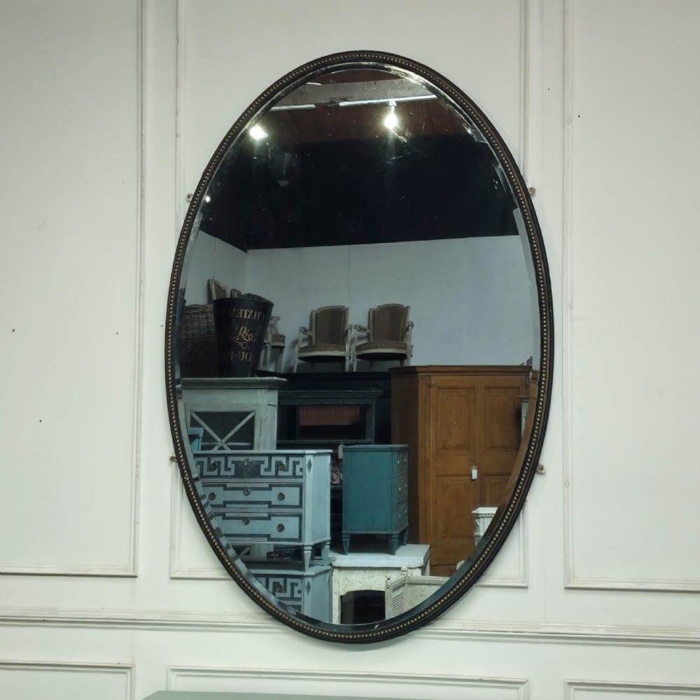 A large, vertical oval wall mirror featuring a gilt frame adorned with a studded beaded border.