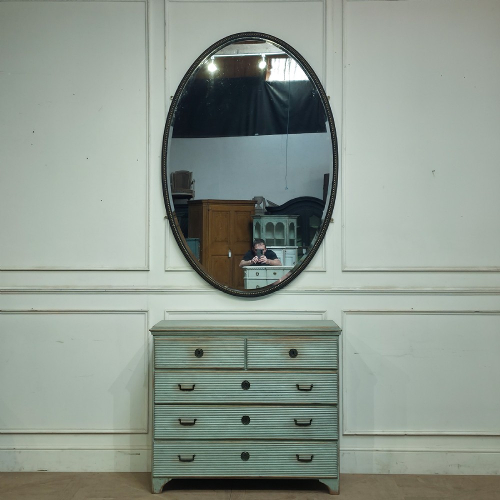 A large, vertical oval wall mirror featuring a gilt frame adorned with a studded beaded border. View II