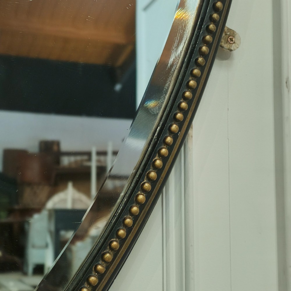 A large, vertical oval wall mirror featuring a gilt frame adorned with a studded beaded border. View III