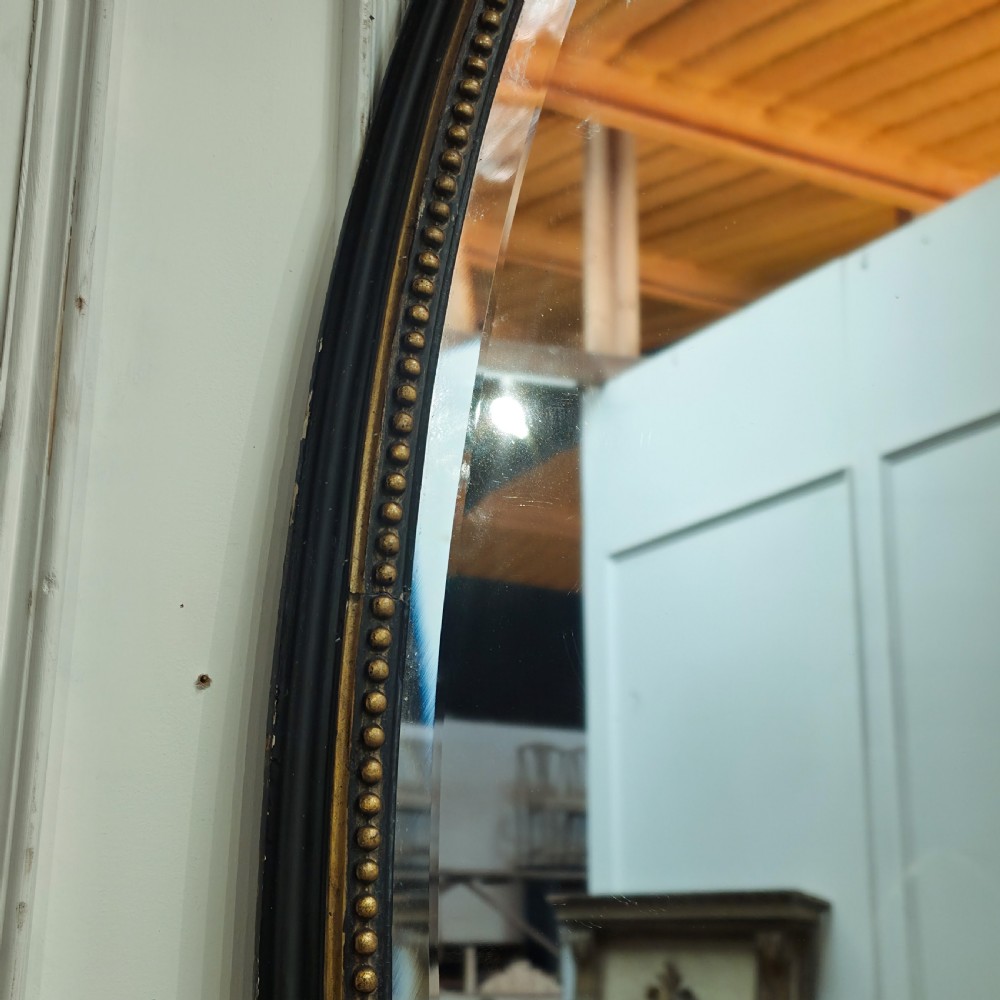 A large, vertical oval wall mirror featuring a gilt frame adorned with a studded beaded border. View IV