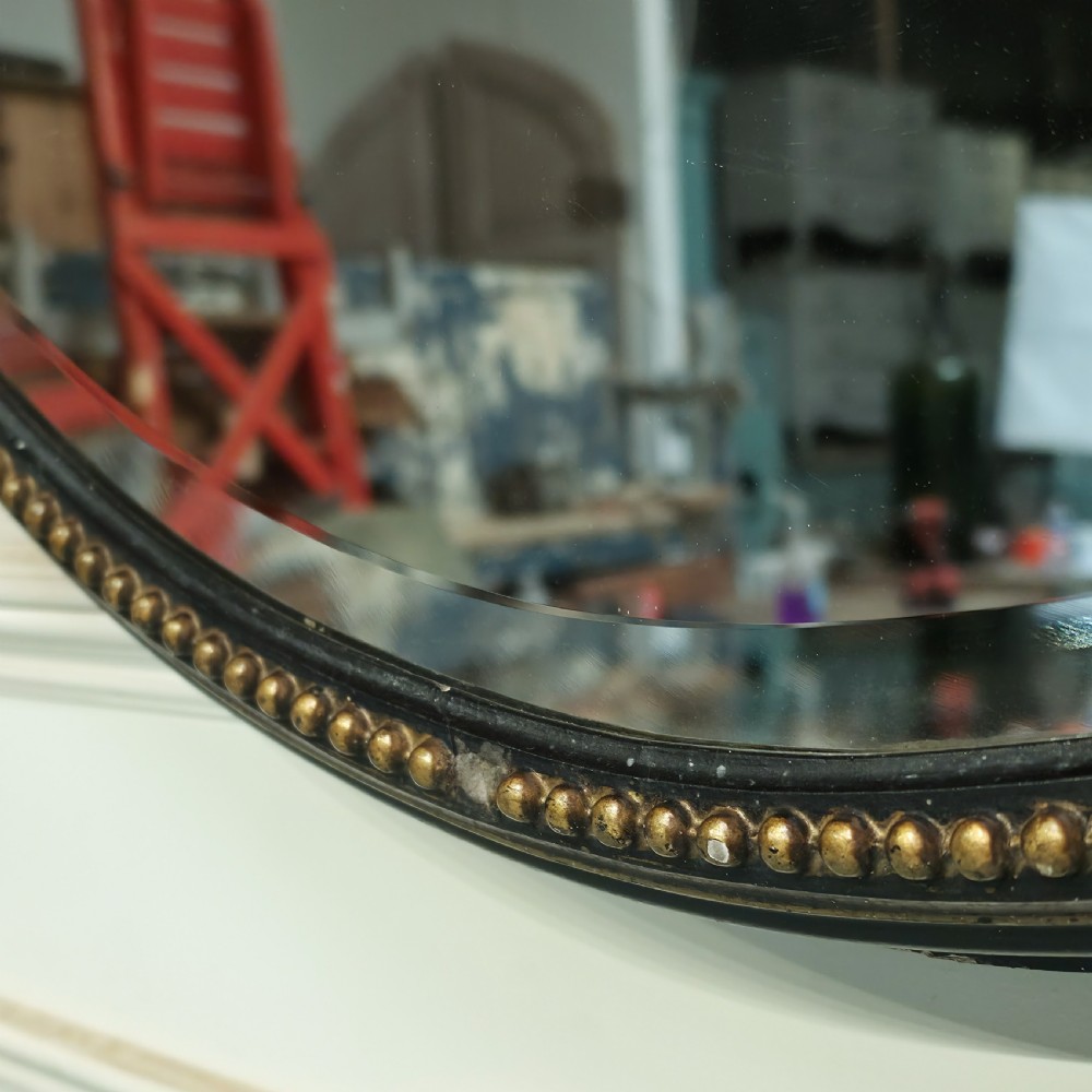 A large, vertical oval wall mirror featuring a gilt frame adorned with a studded beaded border. View V