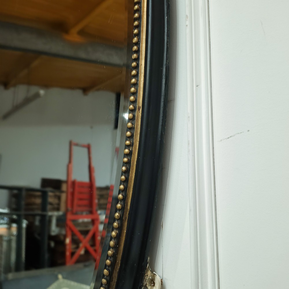 A large, vertical oval wall mirror featuring a gilt frame adorned with a studded beaded border. View VI