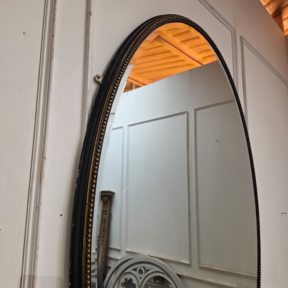 A large, vertical oval wall mirror featuring a gilt frame adorned with a studded beaded border. View VII