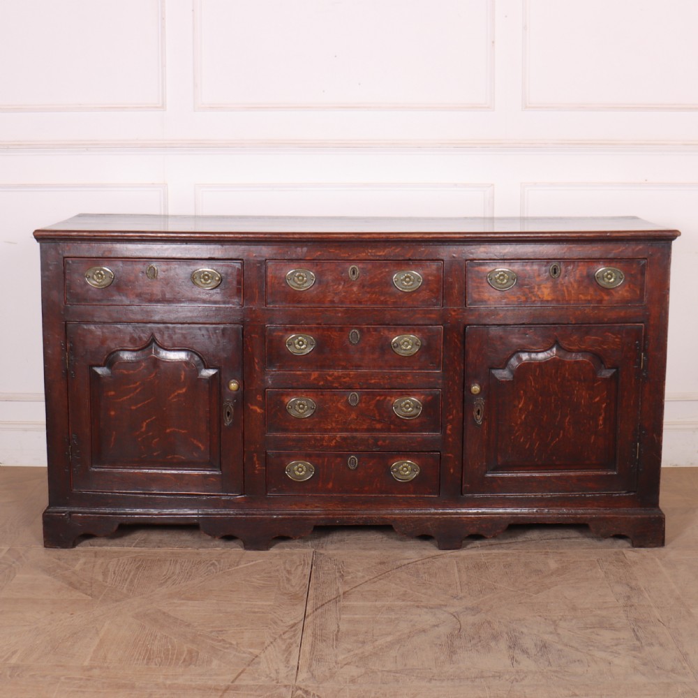 An eighteenth-century dark oak dresser base featuring three top drawers and a central column of drawers flanked by two arched fielded panel cupboard doors.