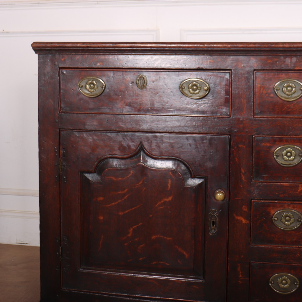 An eighteenth-century dark oak dresser base featuring three top drawers and a central column of drawers flanked by two arched fielded panel cupboard doors. View II