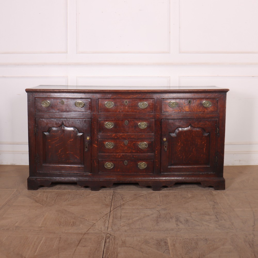 An eighteenth-century dark oak dresser base featuring three top drawers and a central column of drawers flanked by two arched fielded panel cupboard doors. View III