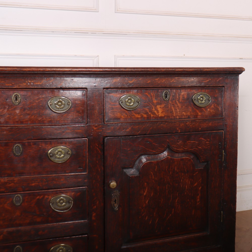 An eighteenth-century dark oak dresser base featuring three top drawers and a central column of drawers flanked by two arched fielded panel cupboard doors. View IV