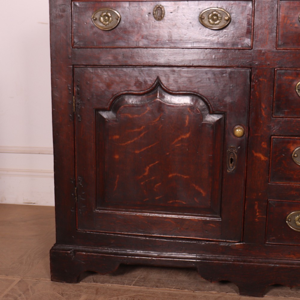 An eighteenth-century dark oak dresser base featuring three top drawers and a central column of drawers flanked by two arched fielded panel cupboard doors. View VI