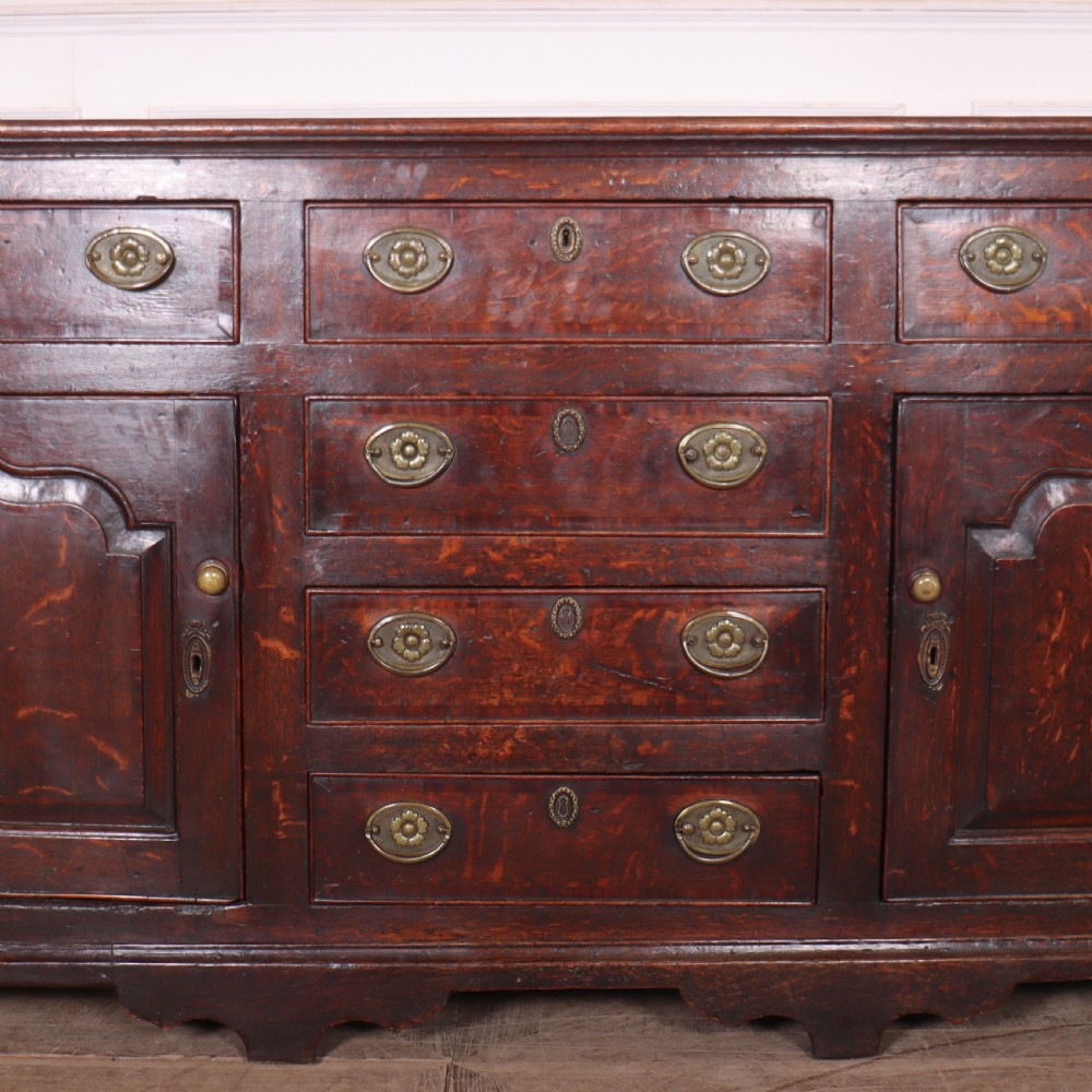An eighteenth-century dark oak dresser base featuring three top drawers and a central column of drawers flanked by two arched fielded panel cupboard doors. View VII