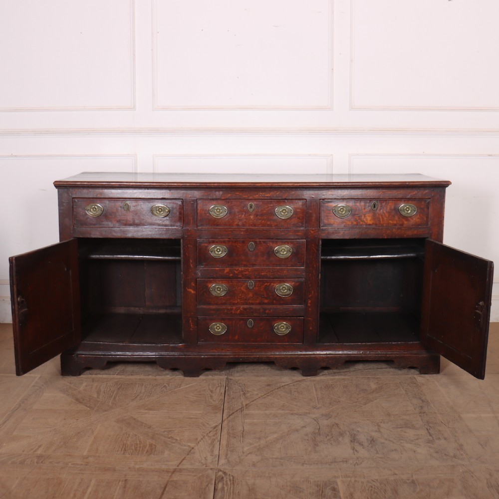 An eighteenth-century dark oak dresser base featuring three top drawers and a central column of drawers flanked by two arched fielded panel cupboard doors. View VIII