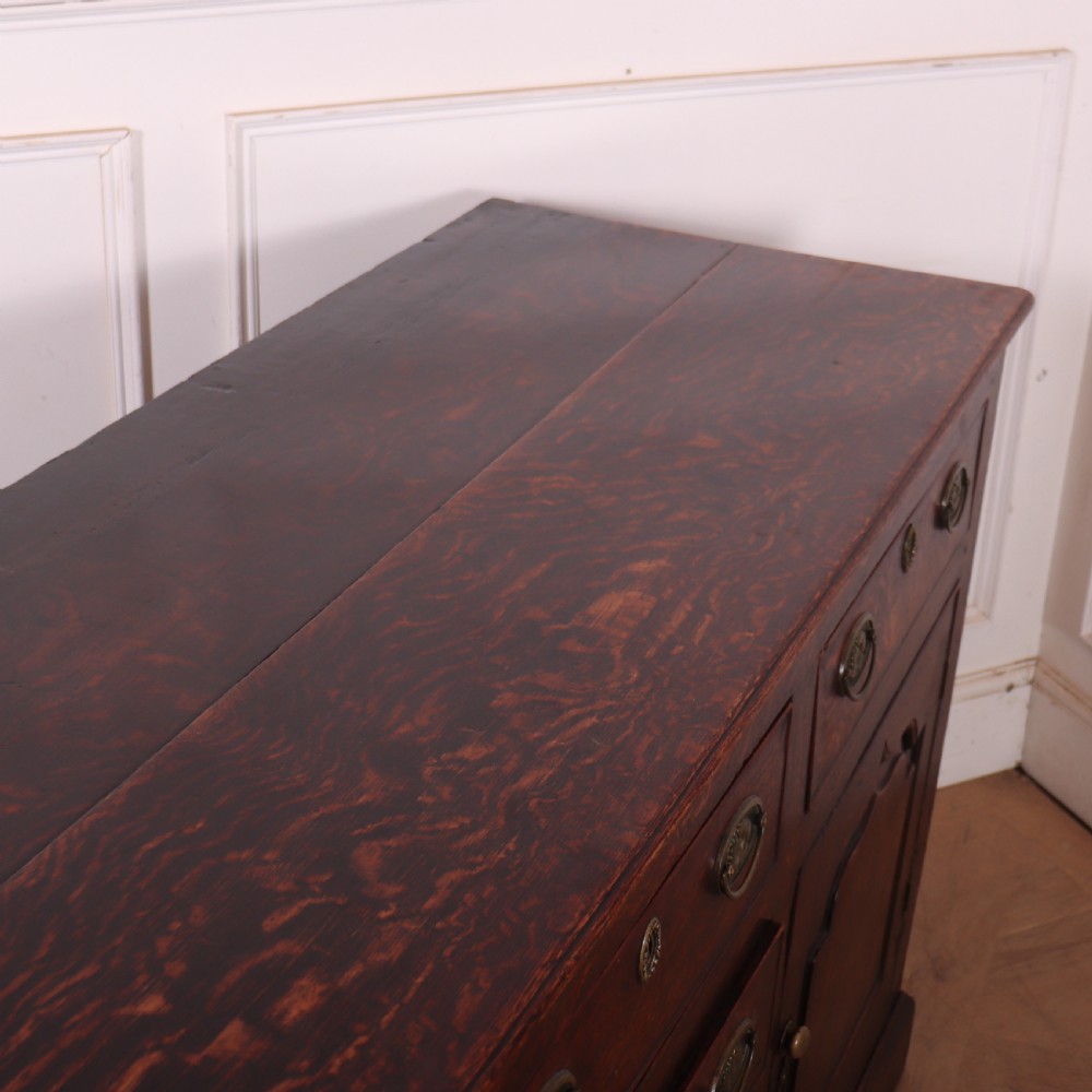 An eighteenth-century dark oak dresser base featuring three top drawers and a central column of drawers flanked by two arched fielded panel cupboard doors. View XI