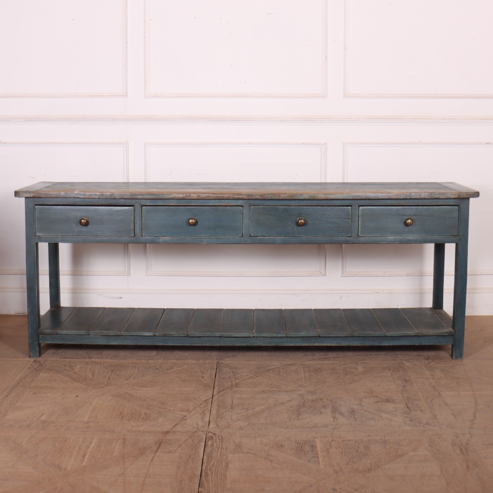 A long muted blue painted wooden dresser base featuring four drawers with brass knobs, a exposed wood top surface, and an open slatted lower shelf.