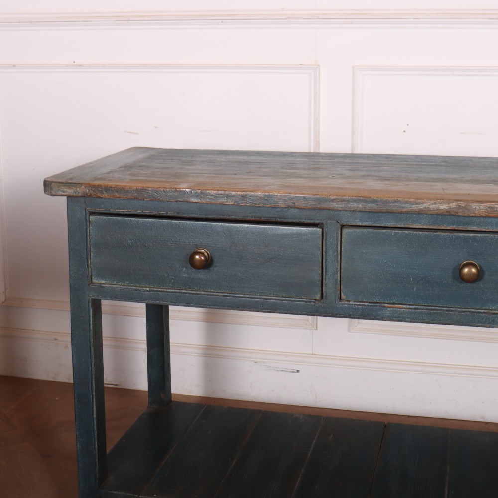 A long muted blue painted wooden dresser base featuring four drawers with brass knobs, a exposed wood top surface, and an open slatted lower shelf. View II