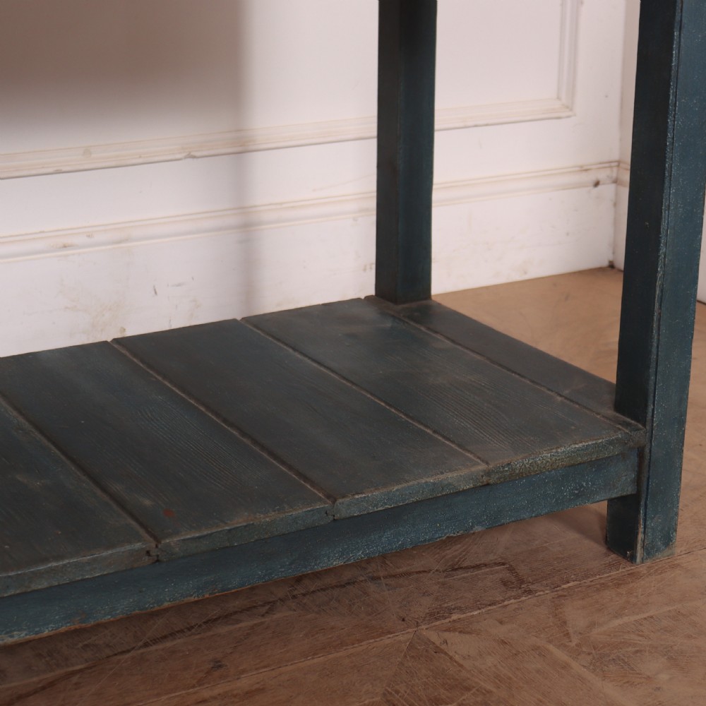 A long muted blue painted wooden dresser base featuring four drawers with brass knobs, a exposed wood top surface, and an open slatted lower shelf. View V