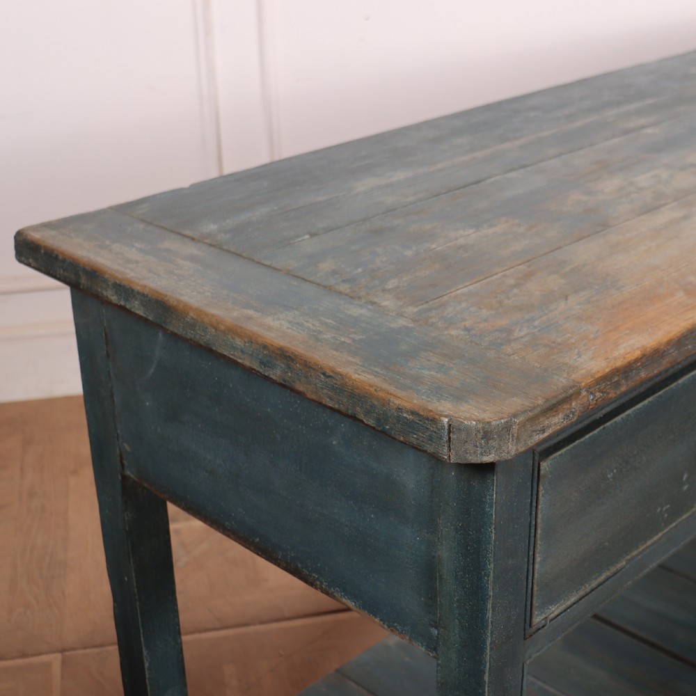 A long muted blue painted wooden dresser base featuring four drawers with brass knobs, a exposed wood top surface, and an open slatted lower shelf. View VII