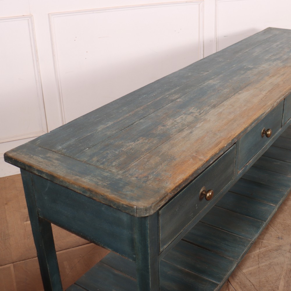 A long muted blue painted wooden dresser base featuring four drawers with brass knobs, a exposed wood top surface, and an open slatted lower shelf. View VIII